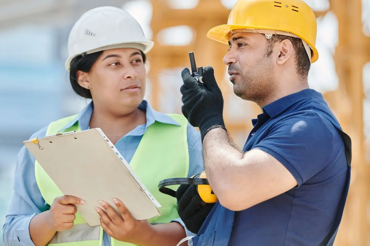 Deux professionnels du bâtiment en casque consultent les plans sur un chantier