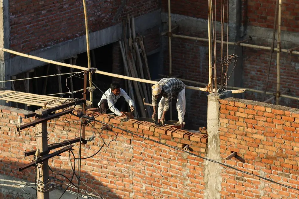 Deux maçons élevant un mur en briques au soleil